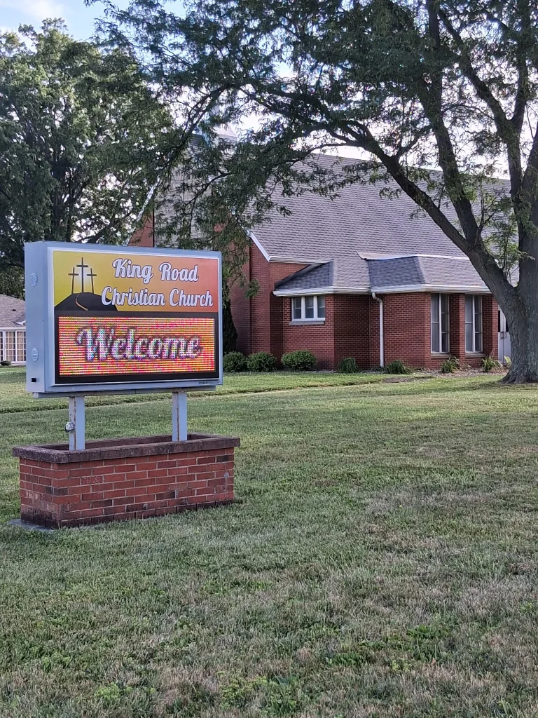 The King Road Christian Church sign displaying Welcome, with the church and trees behind it